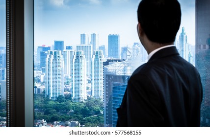 Business Man Looking To City Skyline Through Window Of Skyscraper Office Building 