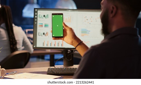 Business Man Looking At Greenscreen Display On Mobile Phone, Working In Office At Night. Using Isolated Chroma Key Background With Blank Copyspace And Mockup Template On Smartphone.