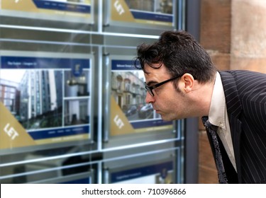 A Business Man Looking At Houses / Flat For Sale In Estate Agent Window.