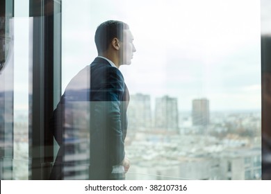 Business man looking out through the office balcony seen through glass doors.