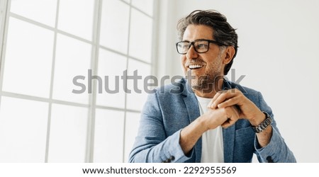 Business man looking outside the window in an office. Senior business man thinking about work while sitting at his desk in a suit.