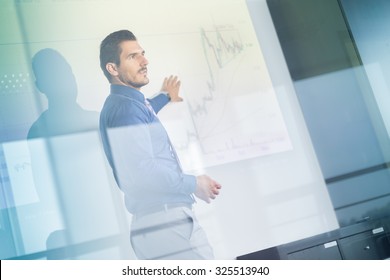 Business man making a presentation in front of whiteboard. Business executive delivering a presentation to his colleagues during meeting or in-house business training. View through glass.