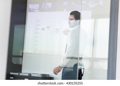 Business Man Making A Presentation In Front Of Whiteboard. View Through Glass.