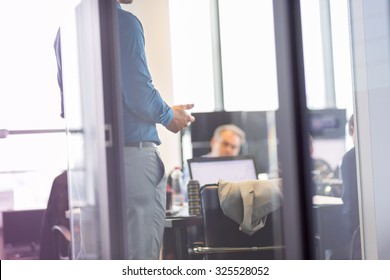 Business Man Making A Presentation At Office. Business Executive Delivering A Presentation To His Colleagues During Meeting Or In-house Business Training. View Through Glass.