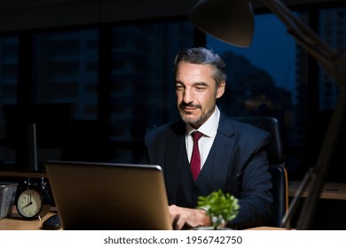 Business Man Office Worker Wear Formal Suit Working At His Desk In The Dark Office At Night. Business Man Working Overtime With Laptop Computer In Lamplight