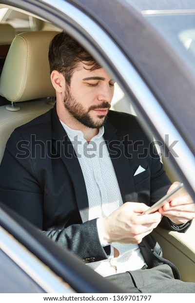 Business man on business trip in the car reads a\
message on his tablet\
pc