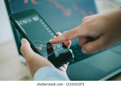 Business man point to the smart phone show financial market chart and Blurred background of a laptop show financial market chart, Stock market concept. - Shutterstock ID 1115151371