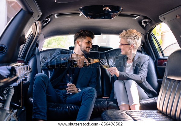 Business man pours champagne to business woman\
in limousine