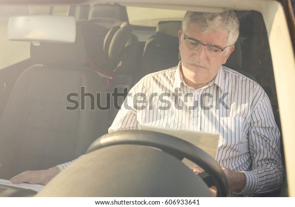 Business man reading a contract
in a car.  Shot through the windshield. Driver partially
visible.