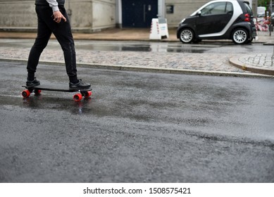 A Business Man Rides An Electric Skateboard Along The Street In Rainy Weather. The Concept Of Portable Personal Transport.