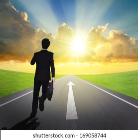 business man running forward on asphalt road with arrow , and beautiful sunset and sunshine, business concept