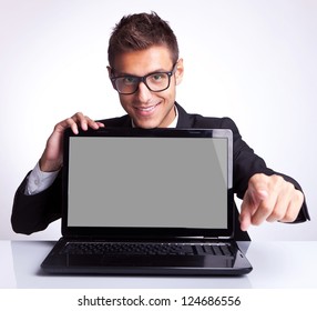 Business Man Sitting At Office Desk With Laptop Computer Facing The Camera And Pointing His Finger To You