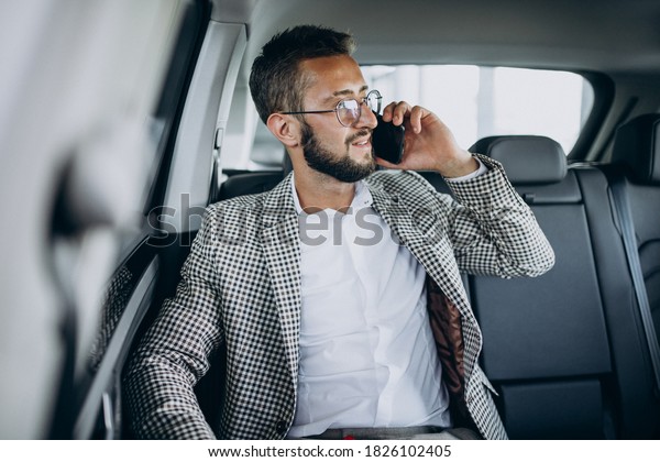 Business man sitting on the back sit of a car\
using tablet