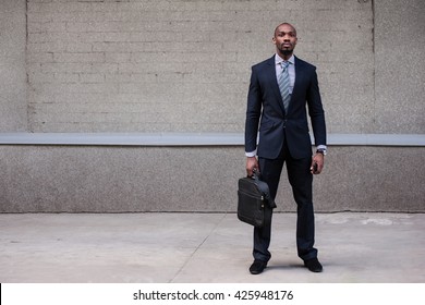 Business Man Standing With A Briefcase And Phone On A Gray Background