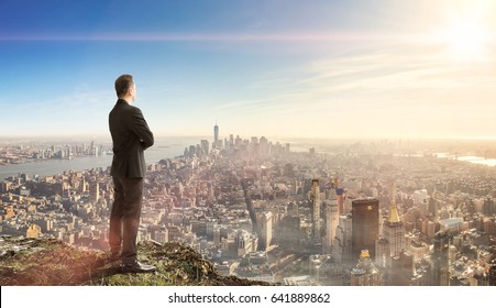 Business Man Standing On Top Mountain Looking Down To The City