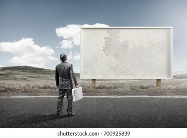 A Business Man Standing And Staring At A Blank Billboard Advertisement.