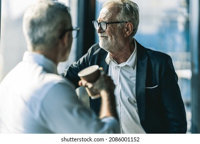 ํYoung Business Man  Talking To His Older Business Partner. They Are In White Shirt And Black Tie. They Are Sitting On A Table In A Hotel Lobby. They Are Holding Their Prefer Drink In Their Hands.