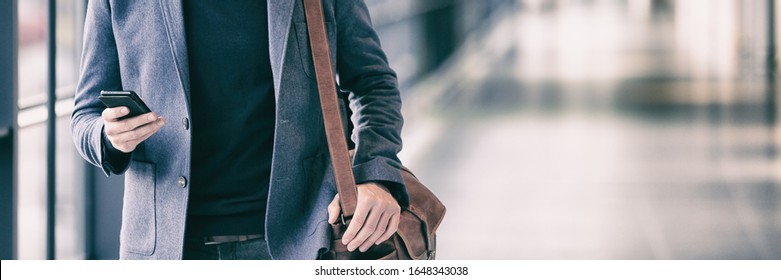 Business man texting using phone walking on travel commute in airport or train station banner panorama. Businessman hand holding cellphone device technology.
