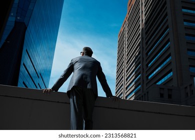Business, man and thinking at city on rooftop about career or future with goal in company. Professional, person and skyscraper on roof is standing with vision or hope for decision as leader at work.