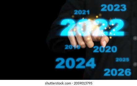 Business man touching a virtual image of New Year's number 2022 in blue on a black background. Scenario of selection, search, beginning of a new era. Determining marketing plans and business growth. - Shutterstock ID 2059013795