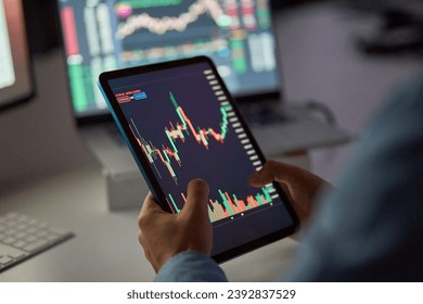 Business man trader broker analyst investor holding tab in hands using digital tablet analyzing stock trade crypto market carts investing finances in stockmarket working in dark night office. Close up