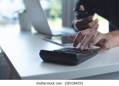 Business Man Using Calculator To Calculate Business Report, E-document On Mobile Phone And Digital Tablet, Working At Modern Office With Laptop Computer On Table, Paperless Office