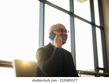 Business man using cell phone while waiting for a flight in airport. Smart Asian man talking on mobile phone with beautiful sunlight.  Smartphone concept.