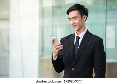 Business Man Using Mobile Phone Outside Of Office In Urban City. Young Asian Man Holding Smartphone For Business Work Or Shopping Online.