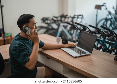 business man using mobile phone while sitting working with laptop in bike shop - Powered by Shutterstock