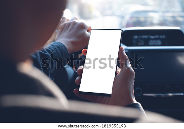Business man using mobile smart phone, checking\
address location via navigator application, driving a car. Driver\
hand holding and looking at cellphone inside a car, white screen\
mockup