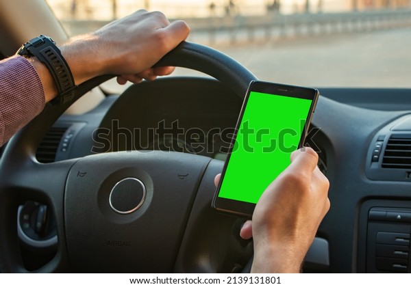 Business man using mobile smart phone, checking\
address location via navigator application, driving a car. Driver\
hand holding and looking at cellphone inside a car, white screen\
mockup.