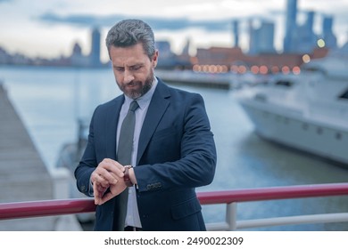 Business man waiting, looks at the clock outdoor. Man in suit checking time on wristwatch. Handsome businessman looking at his watch. Handsome stylish man in suit checking time.