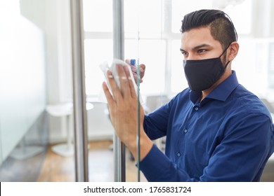 Business Man Wearing Face Mask Because Of Covid-19 With Disinfectant Cleaning Glass In Office