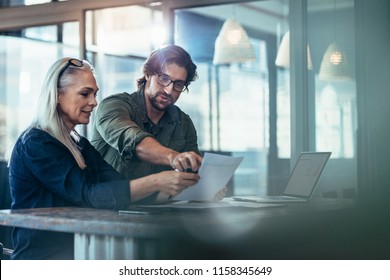 Business man and woman having a meeting in office. Two business colleagues discussing over a report document at work. - Shutterstock ID 1158345649