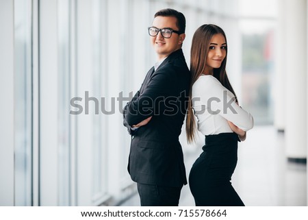 A business man and woman are standing with back to back