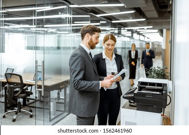 Business Man And Woman Talking Near The Copier During A Coffee Break In The Hallway Of The Big Corporation