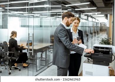 Business man and woman talking near the copier during a coffee break in the hallway of the big corporation