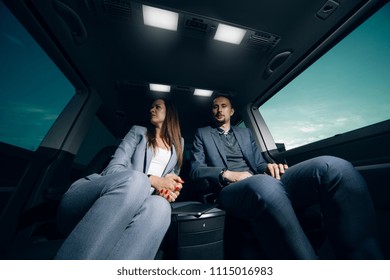 Business Man And Woman Travelling In Vip Car Transfer. Couple At The Back Seats Of Comfortable Van. Rear Seats Row Of Luxury Minivan 