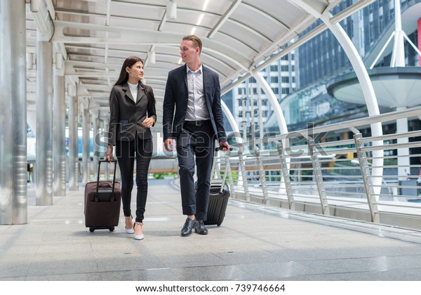 business\
man and business woman wear black suit walk together with luggage\
on the public street, business travel\
concept