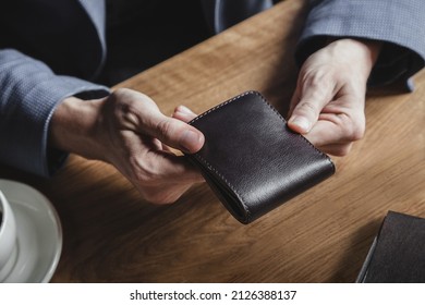 A business man at a wooden table holds a leather wallet in a cafe and waits for a lunch bill. No face, close-up