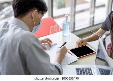 Business Man Workers Wearing Face Mask And Clear Shield Having Discussion Through Glass Partition At The Office As Part Of Business In New Normal During The Outbreak Of COVID-19 Or Coronavirus