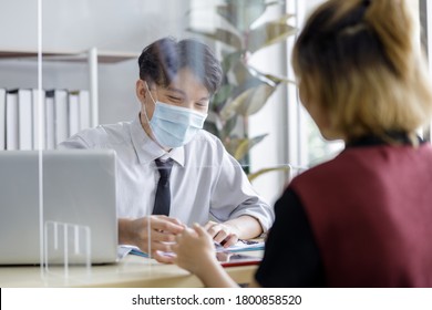 Business Man Workers Wearing Face Mask And Clear Shield Having Discussion Through Glass Partition At The Office As Part Of Business In New Normal During The Outbreak Of COVID-19 Or Coronavirus