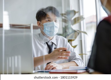 Business Man Workers Wearing Face Mask And Clear Shield Having Discussion Through Glass Partition At The Office As Part Of Business In New Normal During The Outbreak Of COVID-19 Or Coronavirus