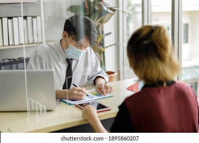 Business Man Workers Wearing Face Mask And Clear Shield Having Discussion Through Glass Partition At The Office As Part Of Business In New Normal During The Outbreak Of COVID-19 Or Coronavirus