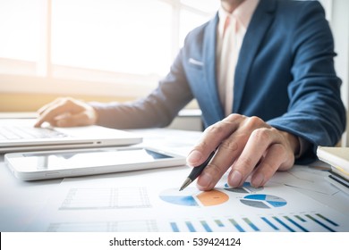 Business Man Working At Office With Laptop, Tablet And Graph Data Documents On His Desk.