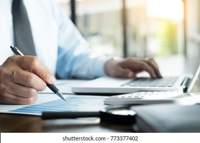Geschäftsmann arbeitet im Büro mit Laptop-, Tablet- und Graphen-Datendokumenten auf seinem Schreibtisch.