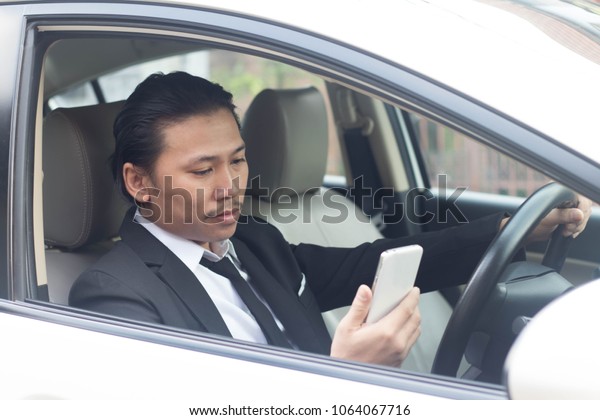 Business man working on business\
car. Young businessman sitting reading a message on a cell\
phone.