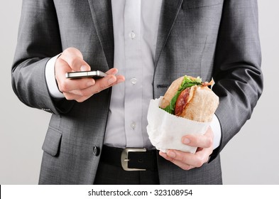 Business Man Working On The Go With Smart Phone And Take Away Sandwich Lunch 