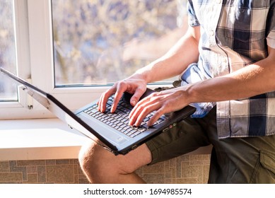 Business Man Working On A Laptop While Sitting On A Windowsill. The Concept Of Remote Work. Self Isolation. Hard Worker. Work At Home. Home Insulation.