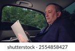 Business man works in car. Politician works looks at information on tablet in car. Man in suit. Serious businessman uses computer tablet to obtain business information in of business car. Automobile